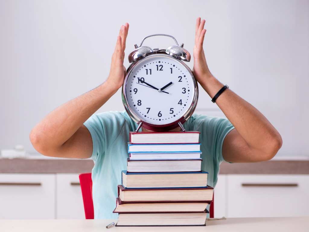 a man with no face sitting at a table filled with books and a giant clock wearing a light blue shirt