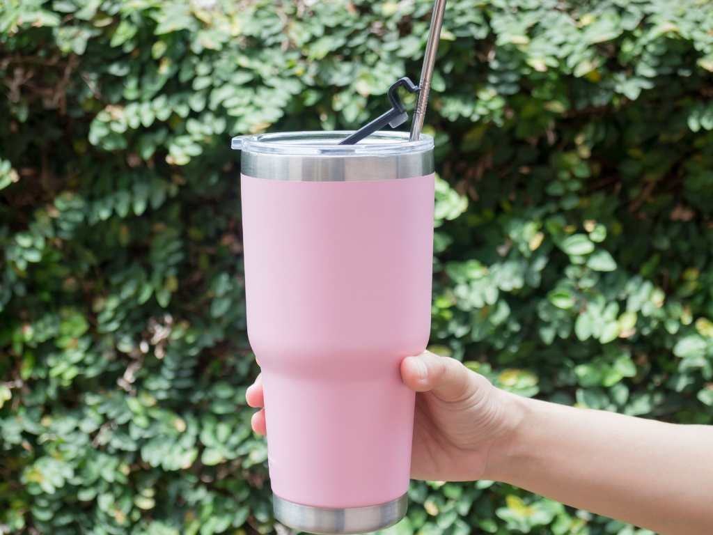 holding out a pink tumbler with a leafy background