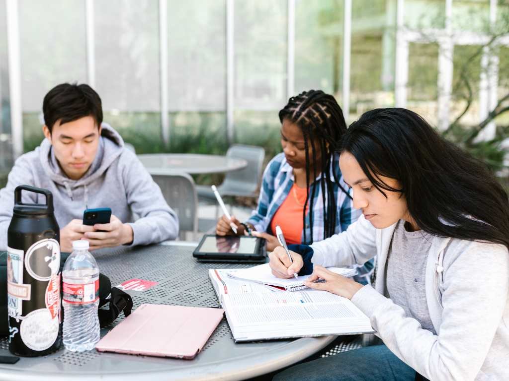 three young people studying on a table wearing jackets