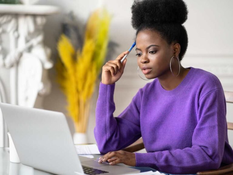 young black woman wearing a purple sweater looking at her laptop