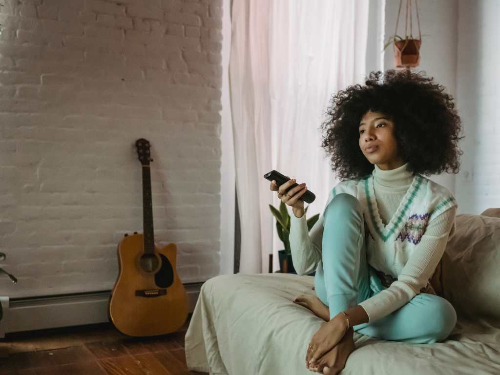 young black woman with an afro flipping through tv with a remote 