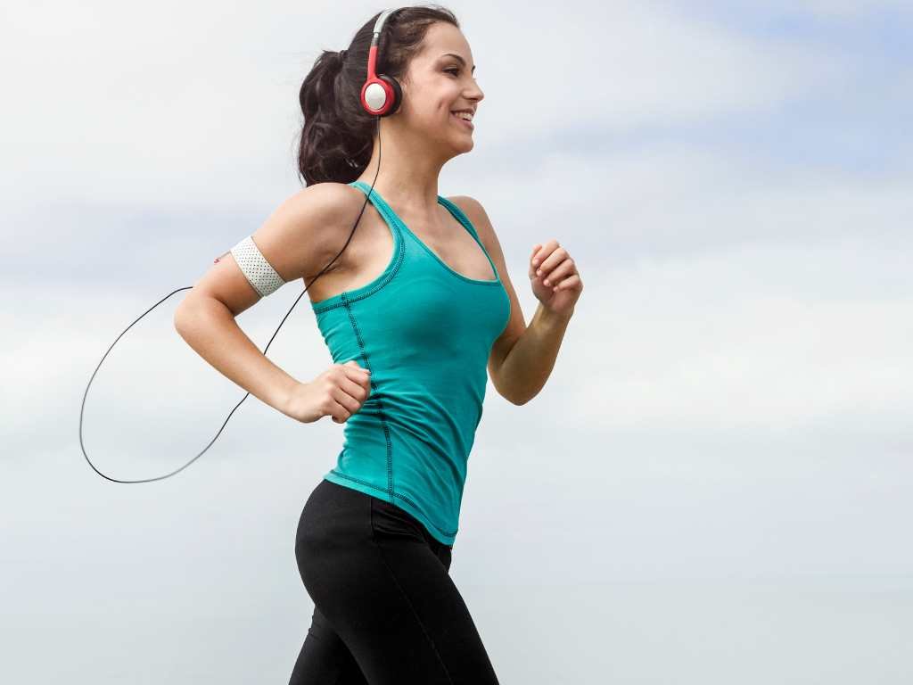 young brunette woman running with headphones in an open field