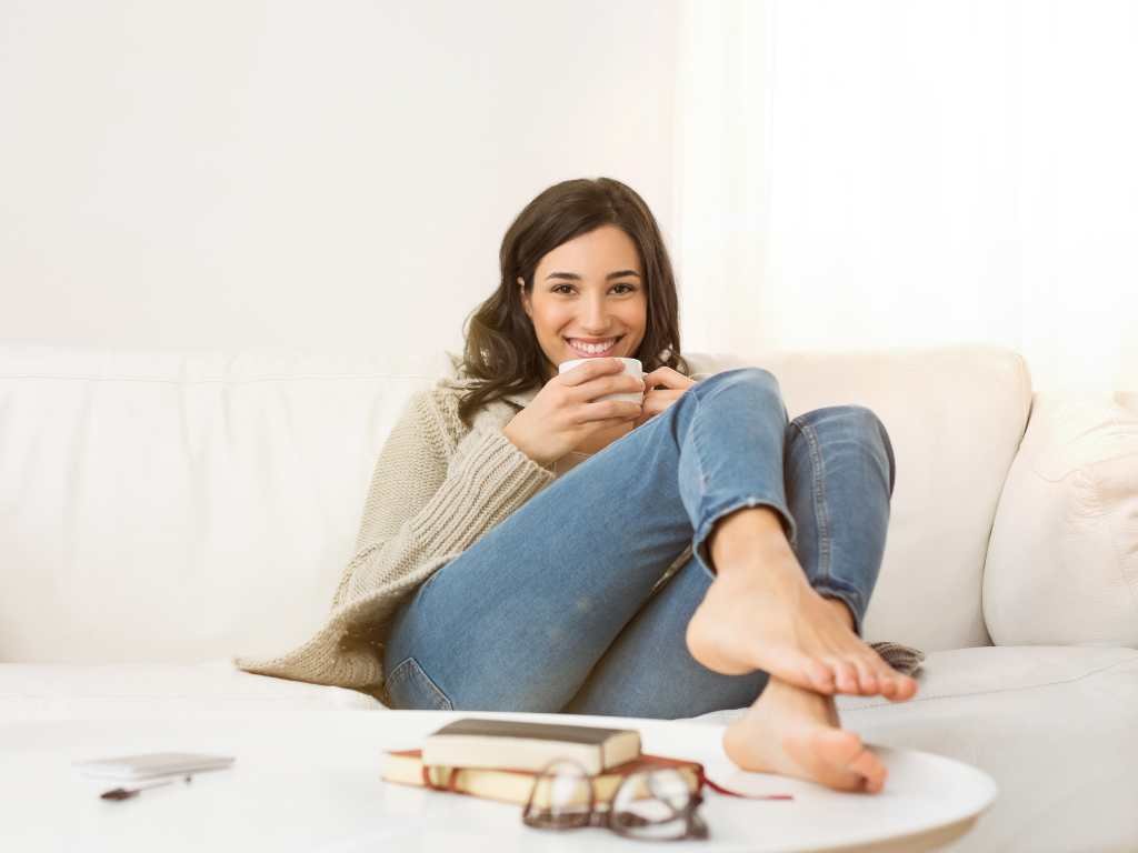 young brunette woman smiling drinking coffee with her feet on top of a white round table