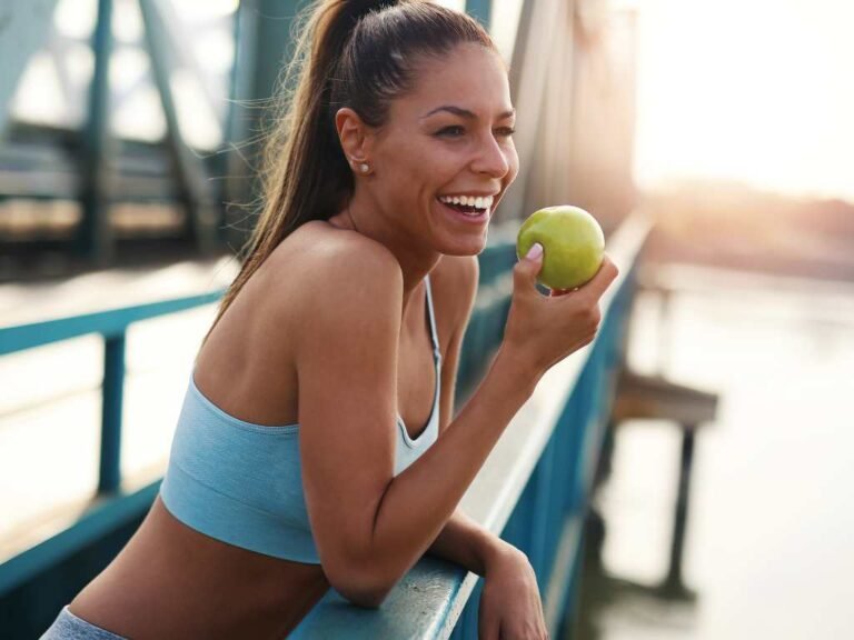 young woman eating a green apple on a bridge wearing an exercise outfit