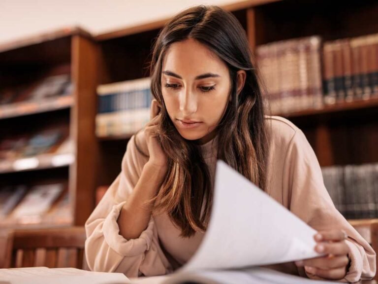 young woman in a library reading her notes at the table