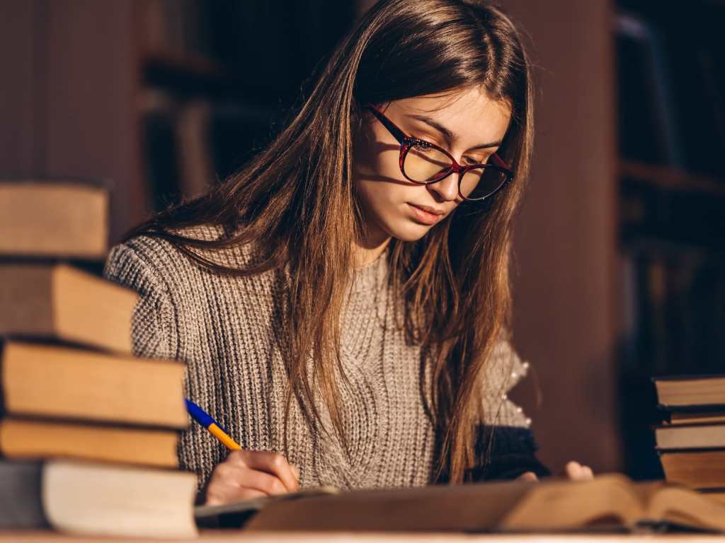 young woman studying with dim light and surrounded by big books