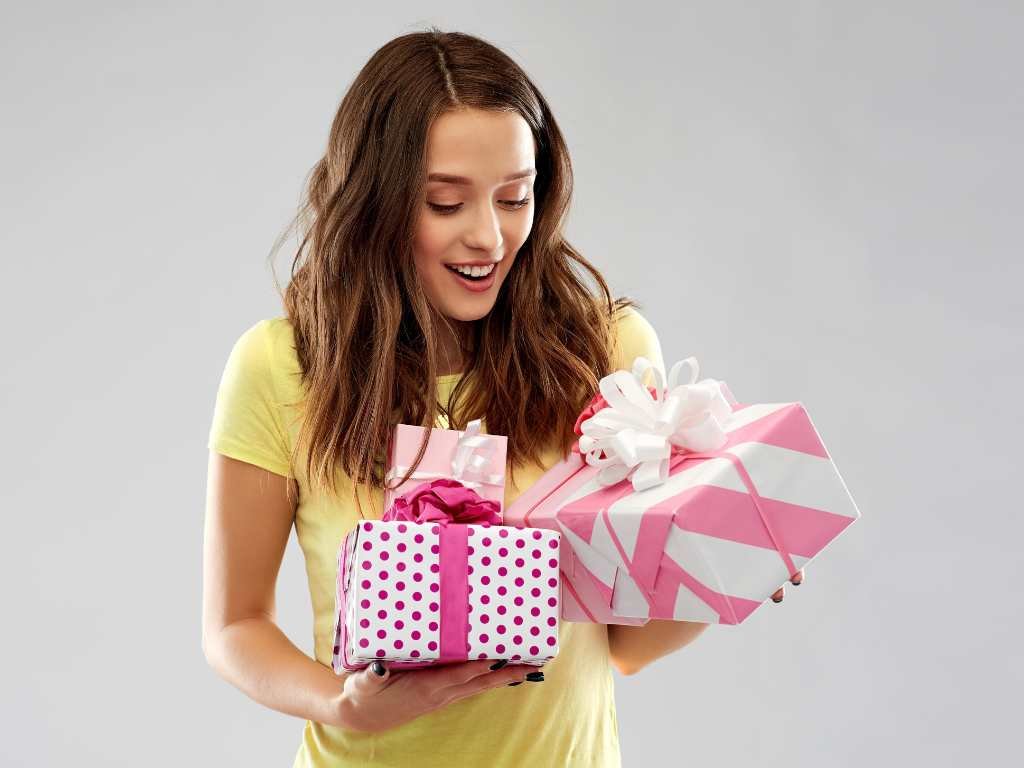 young woman wearing a yellow shirt holding up two gifts in pink and white wrapping paper