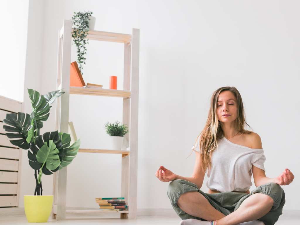 young blonde woman sitting cross-legged on the floor meditating with her eyes closed