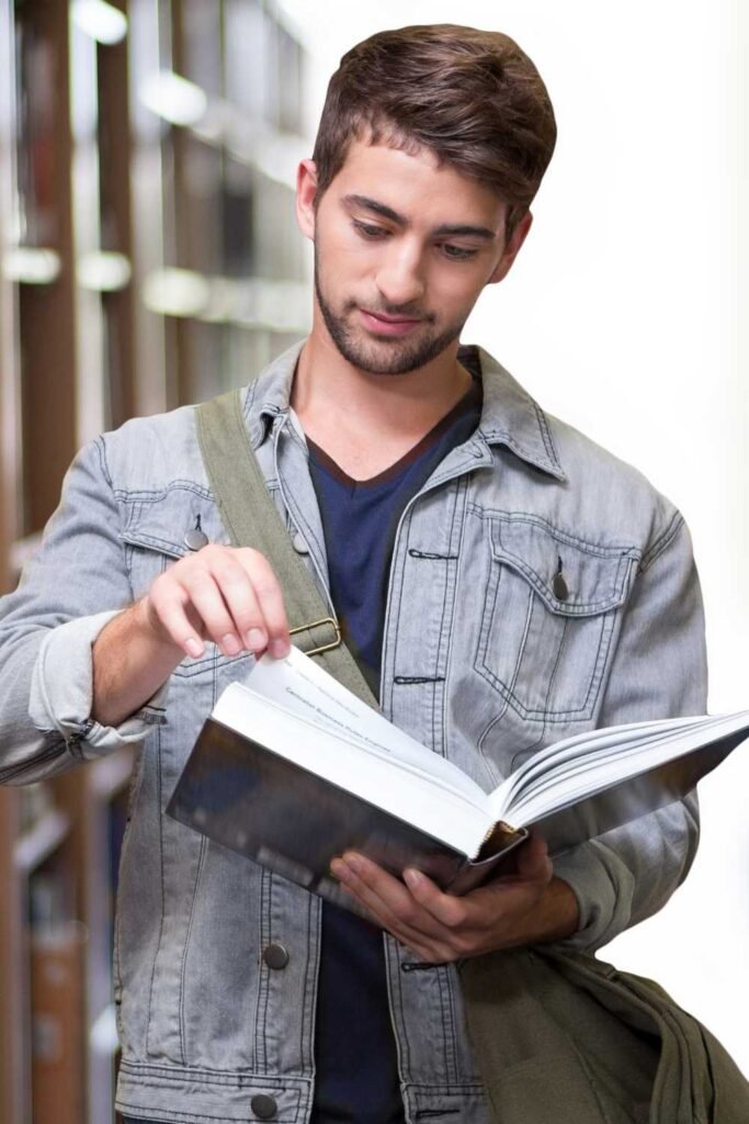 young man in the library reading a book while standing up