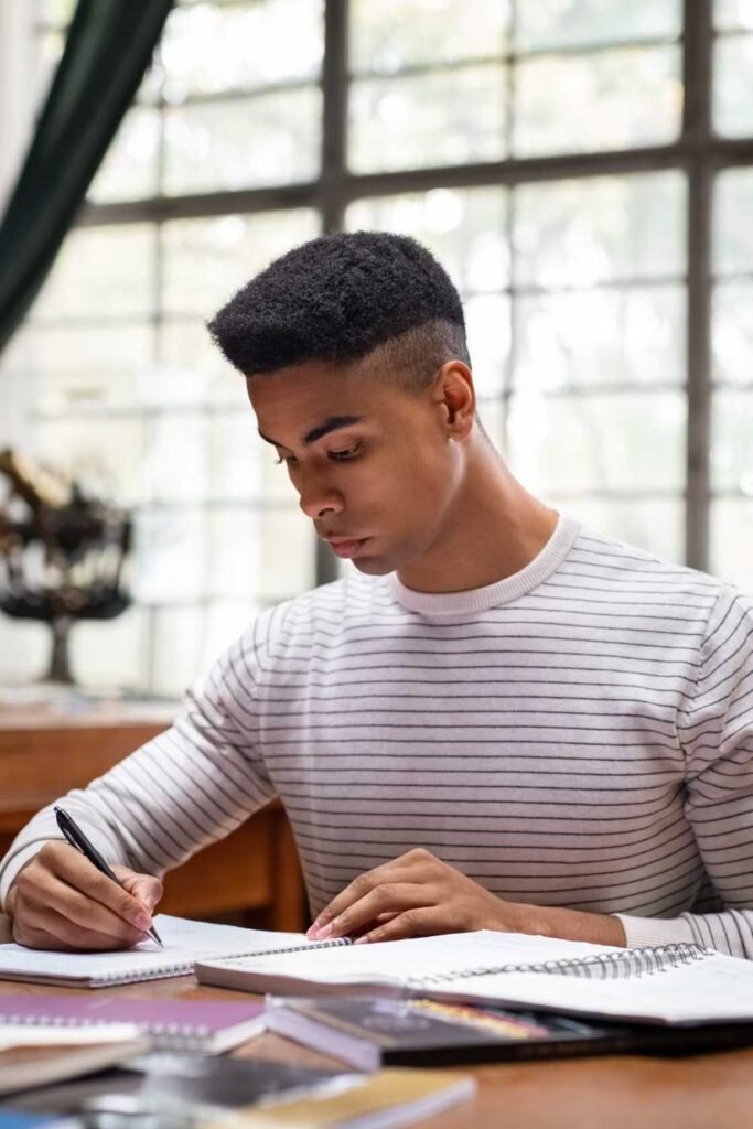 black man writing in his notebook while seated at the library