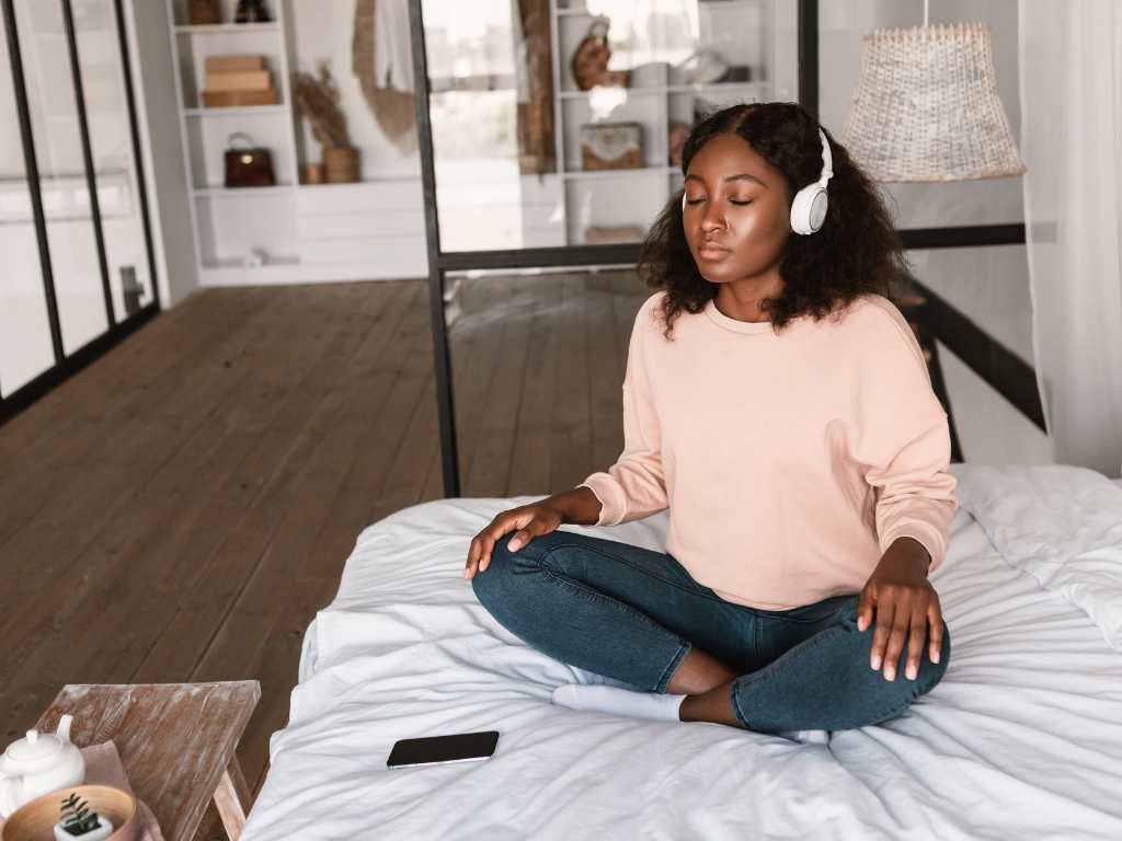 black young woman sitting on her bed with headphones listening to some relaxing music