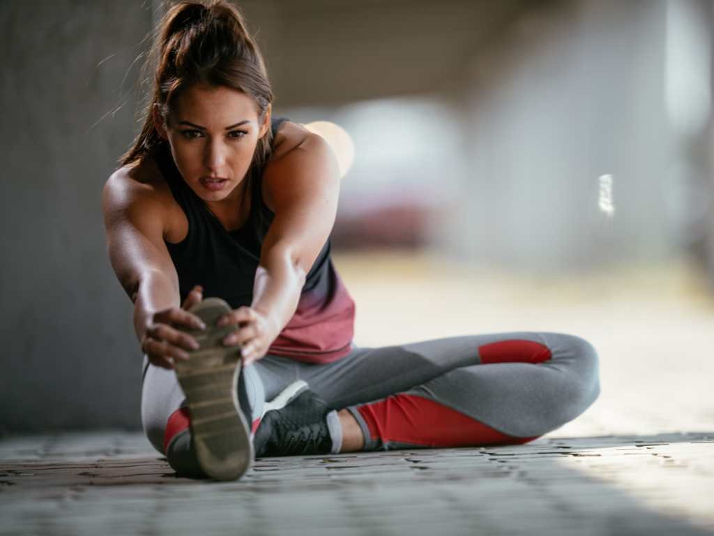 female college student with her hair in a ponytail stretching on the floor