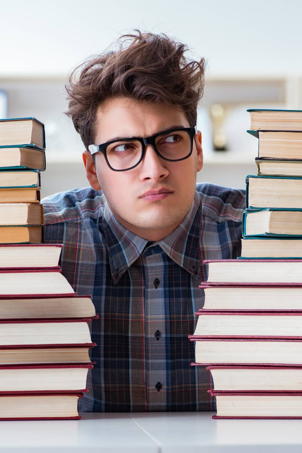A guy wearing eyeglasses sitting between piles of books.