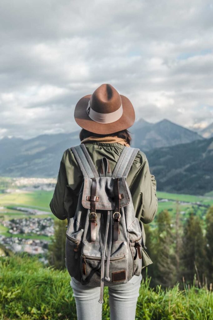young woman with her back facing the camera wearing a backpack and a hat looking at the mountains