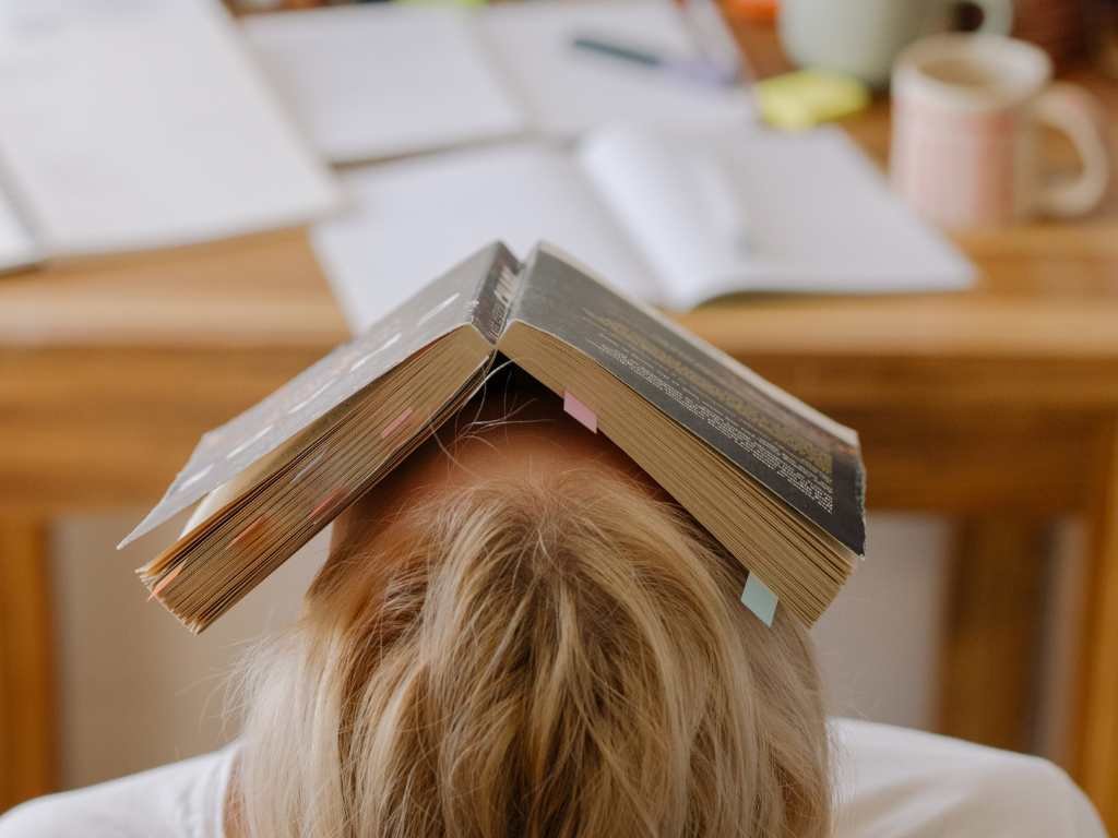 blonde college student stressed out with a book over her face