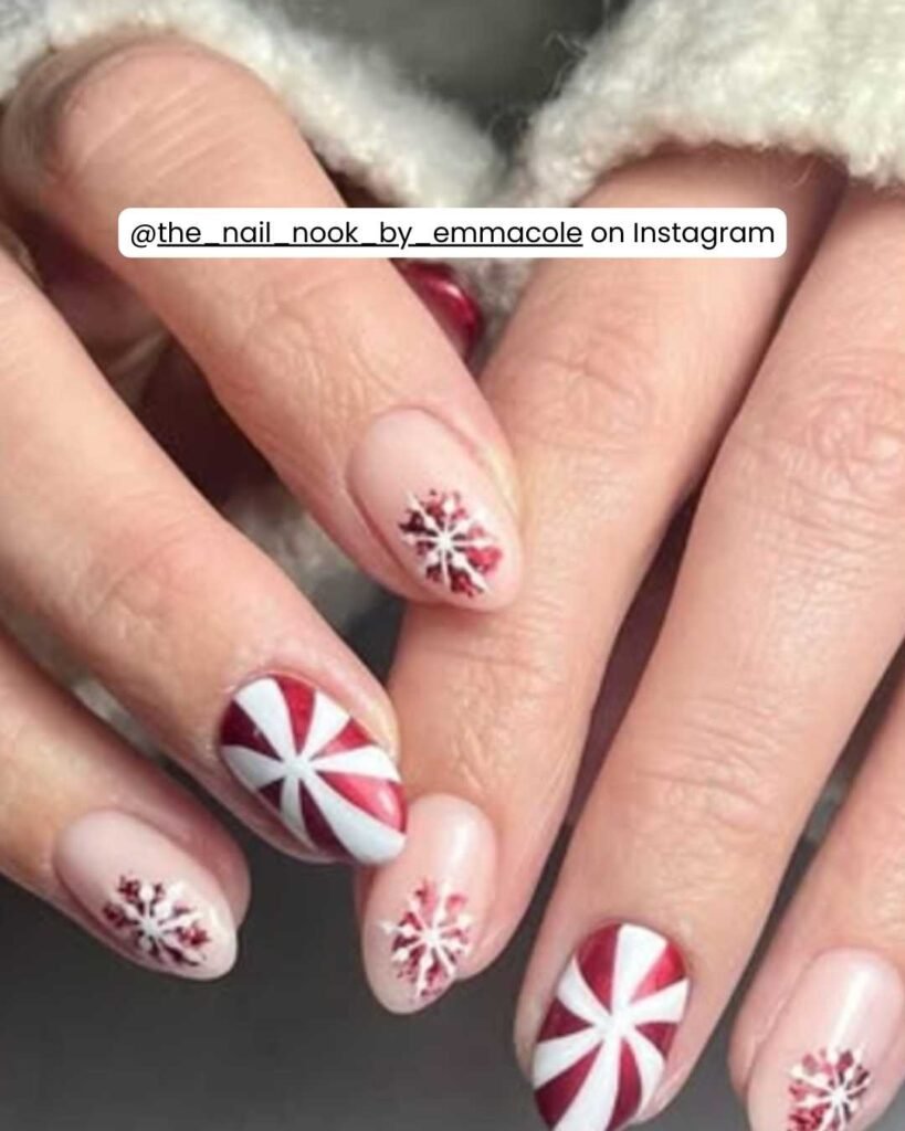 Nude nails with peppermint swirls, delicate snowflakes, bold red accents, and a glossy finish.