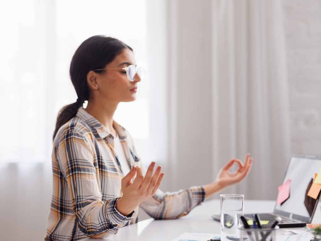 young indian woman with glasses meditating in front of her study table