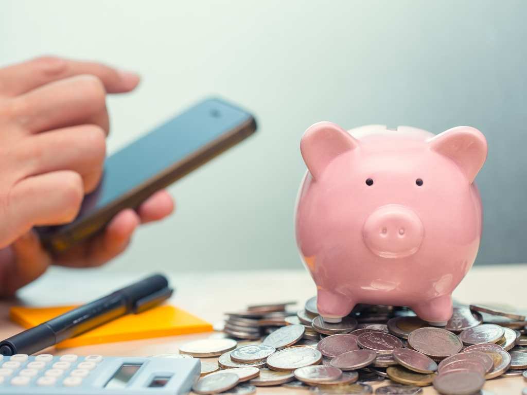 piggy bank with coins underneath with a person holding a cellphone