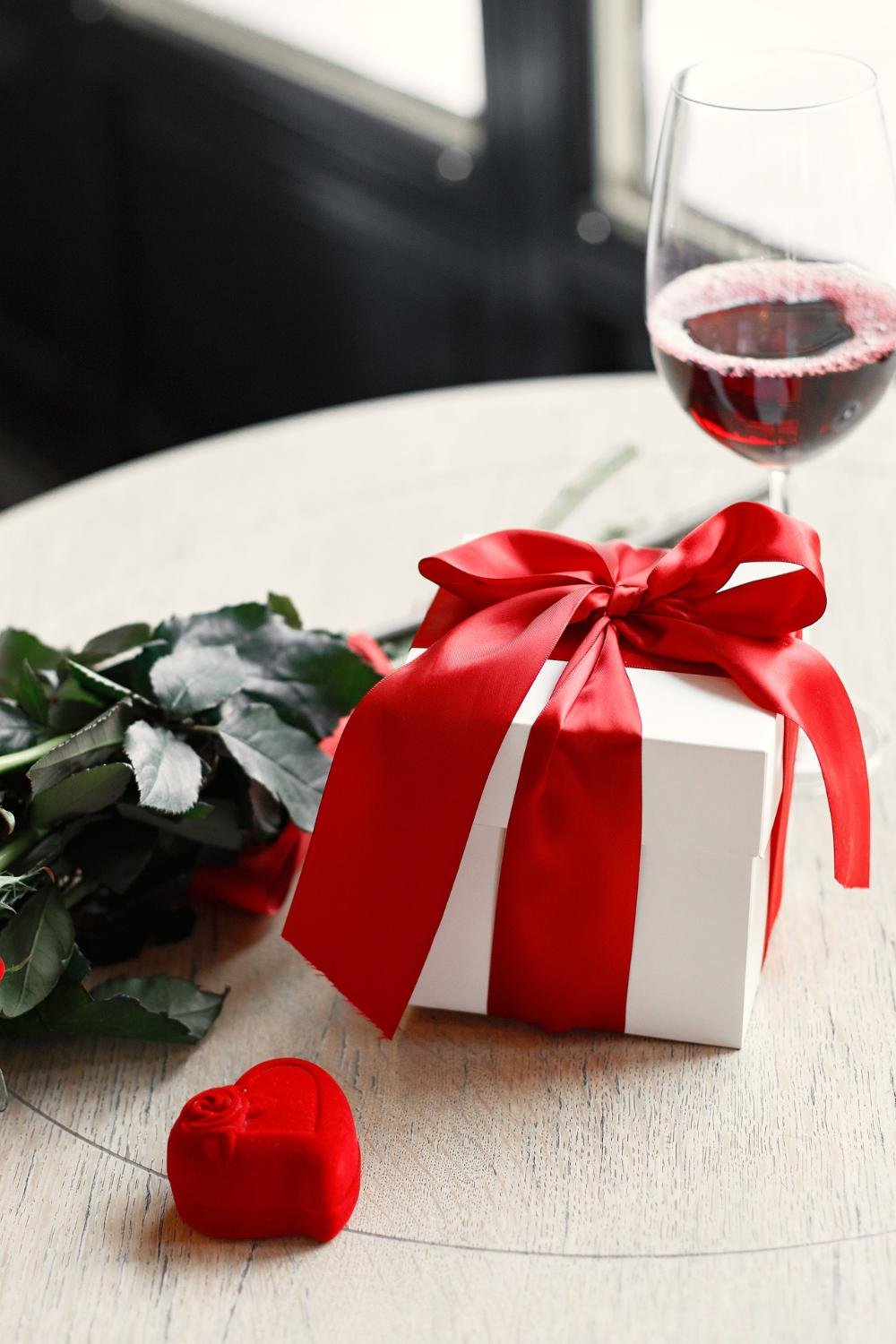 A flower, a gift box, and a bottle of wine arranged on a table.