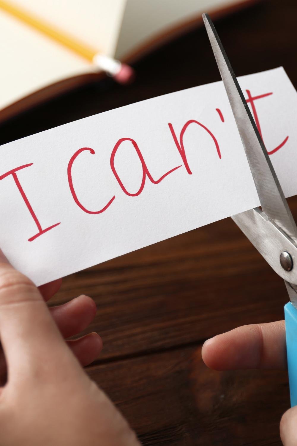 The phrase 'I can't' written on a piece of paper, with scissors positioned as if attempting to cut it.