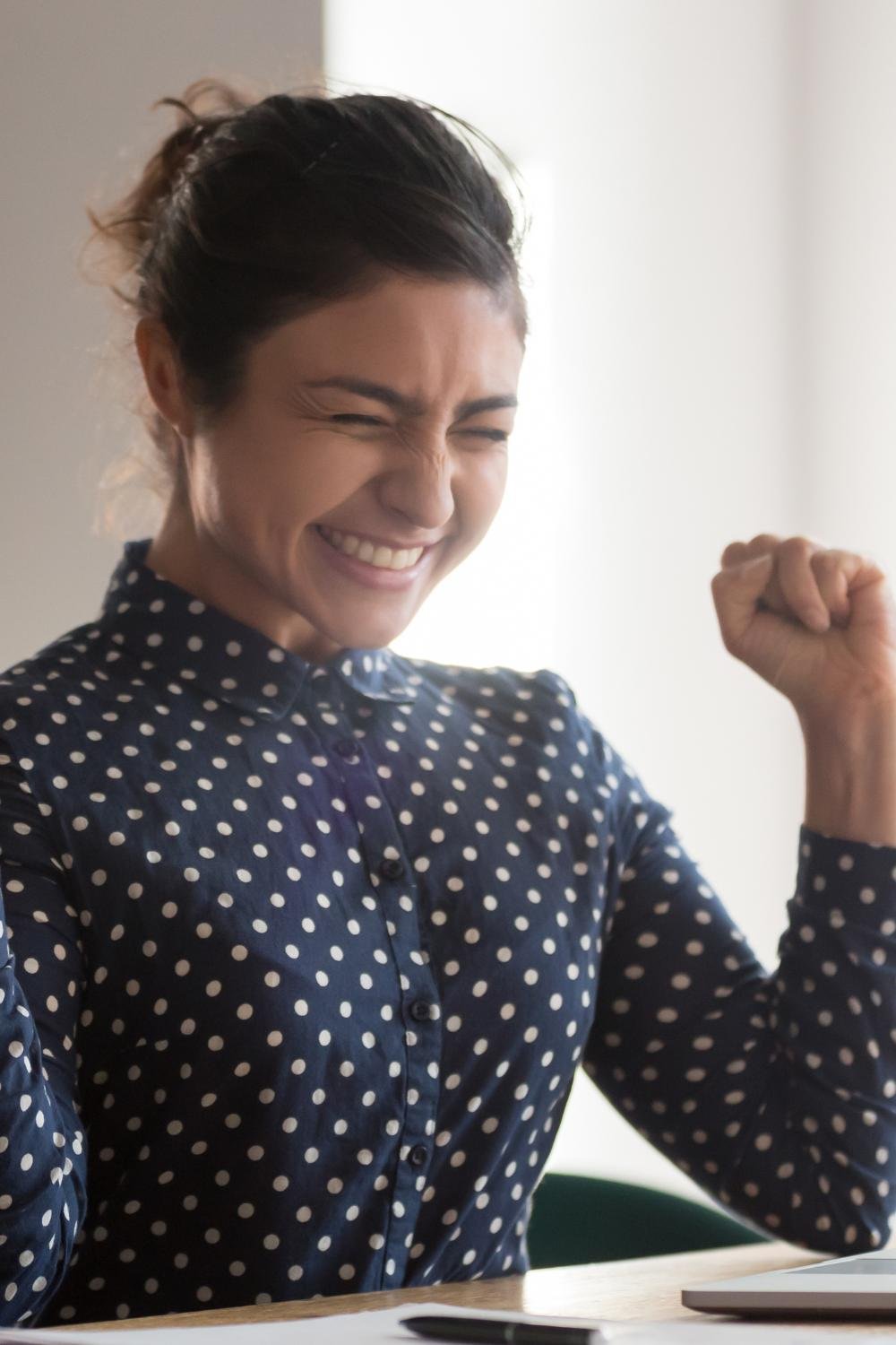 A girl wearing a blue long-sleeve shirt, smiling with her closed fists raised in a celebratory gesture.