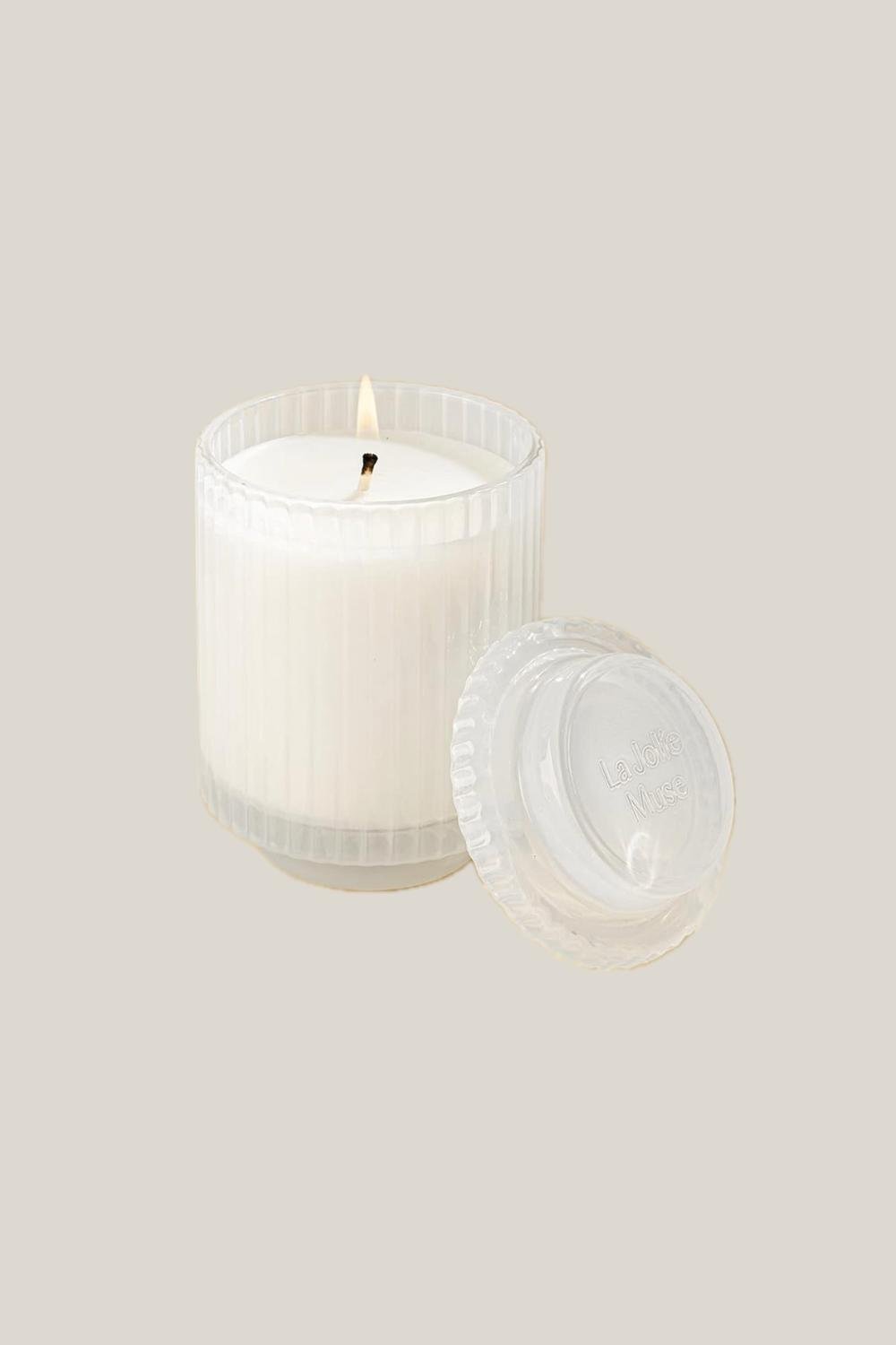 A white scented candle with a lit flame.