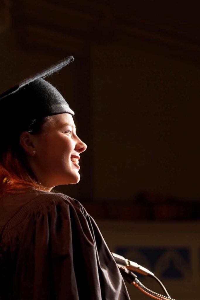 young woman wearing a black toga and graduation hat making a speech at the podium