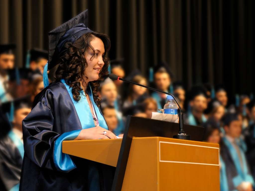 young woman giving a speech on graduation day at the podium and wearing a toga